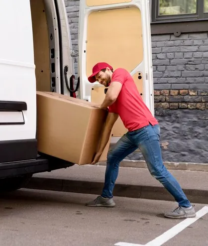 A mover pushing a large box into the back of a white van on a town street